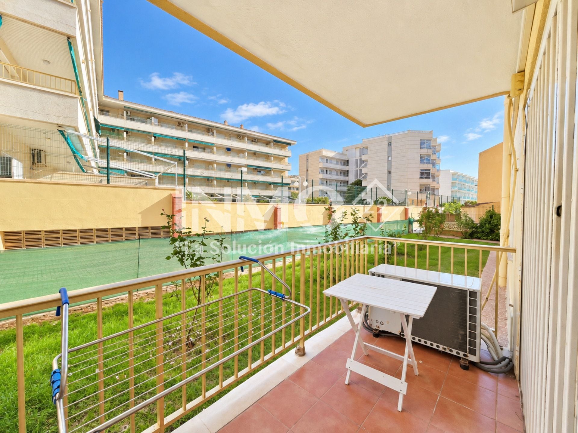 An outdoor balcony with a view of a tennis court, a metal railing, and a small table.