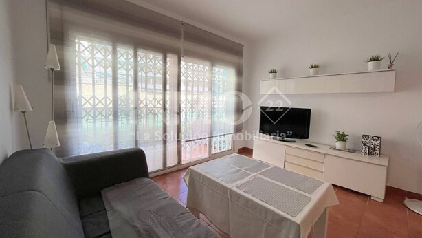 Ein Wohnzimmer mit einer Couch, einem Fernseher auf einem Schrank, einem Tisch mit Tischdecke und einem Balkon mit Blick.
