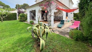 Ein zweistöckiges Haus mit Terrasse, Garten und einer großen Pflanze sowie Gartenmöbeln.