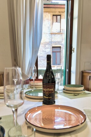 Una mesa de comedor con una botella de vino, copas y platos, con vista a un espacio exterior a través de una ventana.