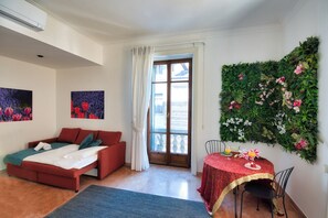 Una habitación con un sofá rojo, una mesa de comedor con mantel rojo y un conjunto de plantas verdes colgadas en la pared.