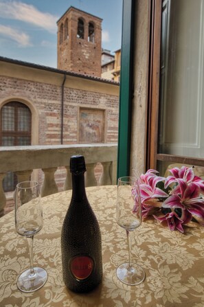 Una botella de vino sobre una mesa con dos copas, un ramo de flores y vista a un edificio de ladrillo con una torre.