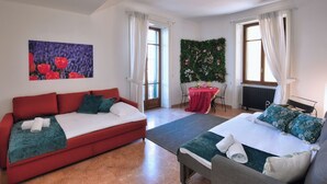 Et værelse med en rød sofa, en seng med grønt sengetøj, et lille bord med et rødt borddække og en væg med blomstermønster.