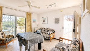 A room with a dining table, two sofas, a ceiling fan, and a view through a glass door. - Apartament with barbecue in La Llosa (Cambrils)