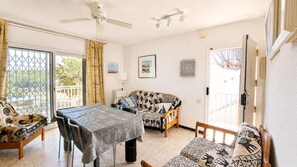 A room with a dining table, two sofas, a ceiling fan, and a view through a glass door. - Apartament with barbecue in La Llosa (Cambrils)