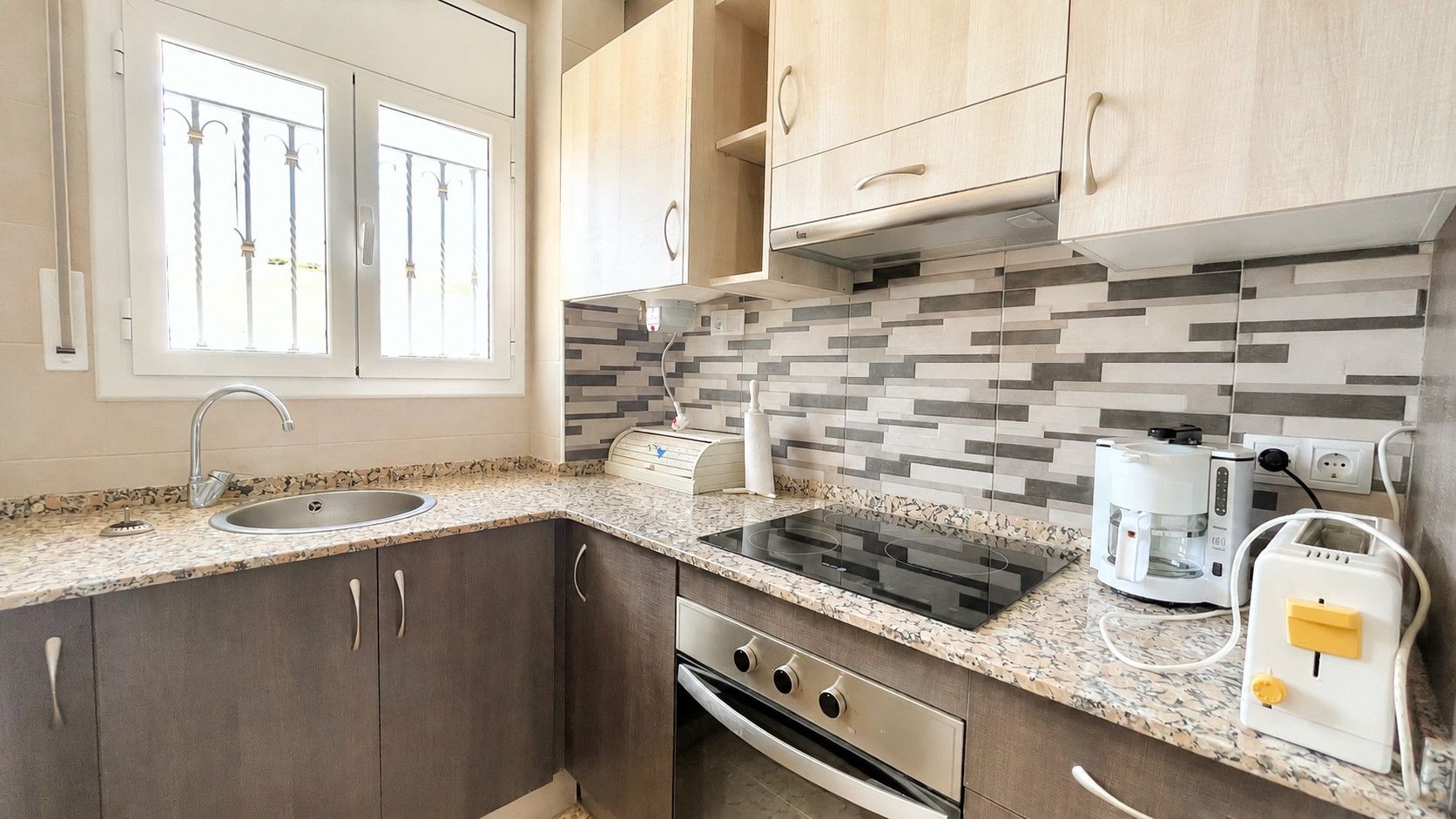 A kitchen with a sink, stove, and coffee maker.