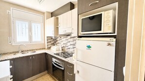 A compact kitchen with a built-in microwave, a refrigerator, a stove, and a sink. - Apartament with barbecue in La Llosa (Cambrils)
