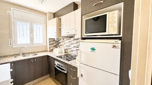 A compact kitchen with a built-in microwave, a refrigerator, a stove, and a sink. - Apartament with barbecue in La Llosa (Cambrils)