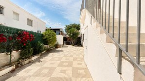 A courtyard with a tiled floor, a white building, and a metal railing. - Apartament with barbecue in La Llosa (Cambrils)