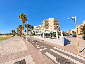 A coastal promenade with a pedestrian walkway, palm trees, and a building with balconies. - Apartamento en 1ra linea (Cambrils)