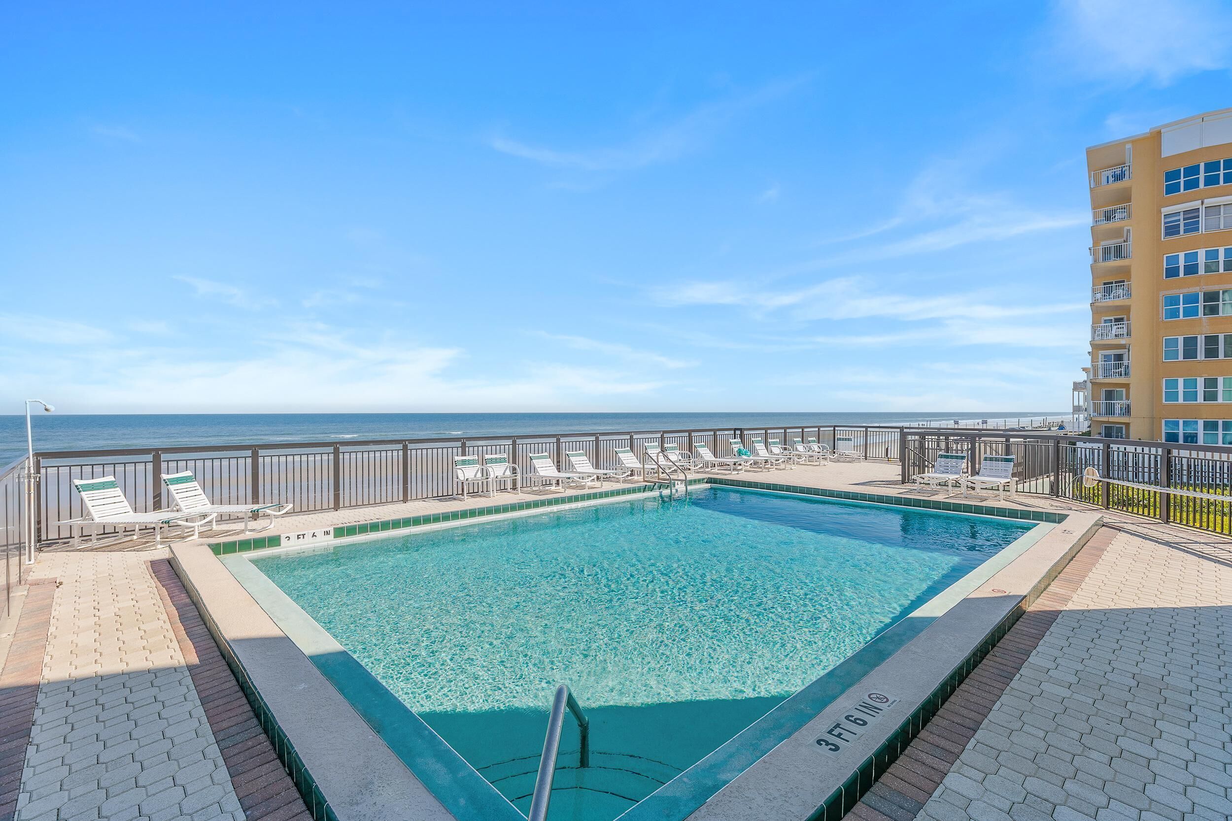 Ein rechteckiger Pool mit klarem, blauem Wasser, umgeben von einer gefliesten Liegefl äche und Liegestühlen.