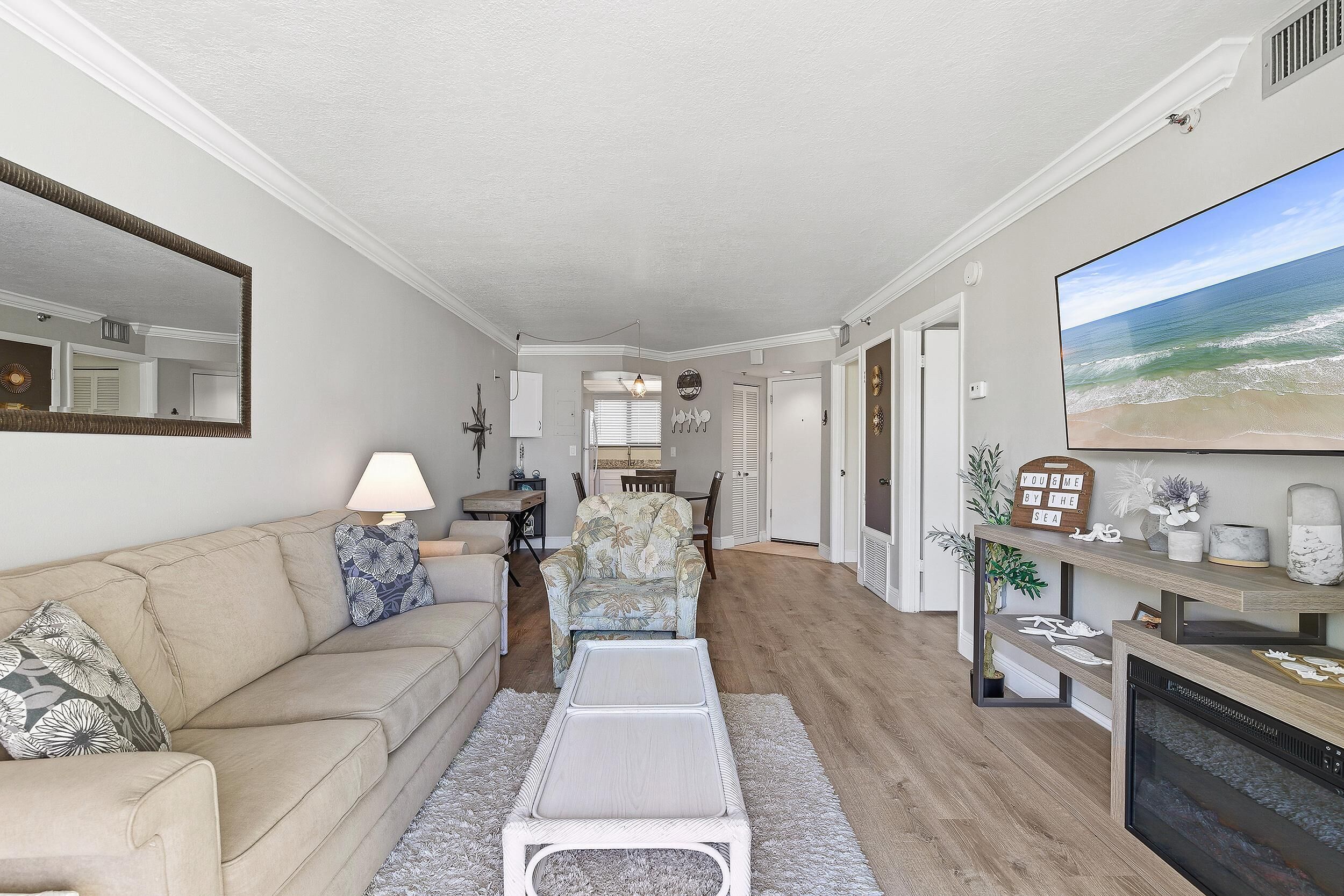 Un salon spacieux avec un canapé beige, une table basse blanche et un téléviseur à écran plat fixé au mur.