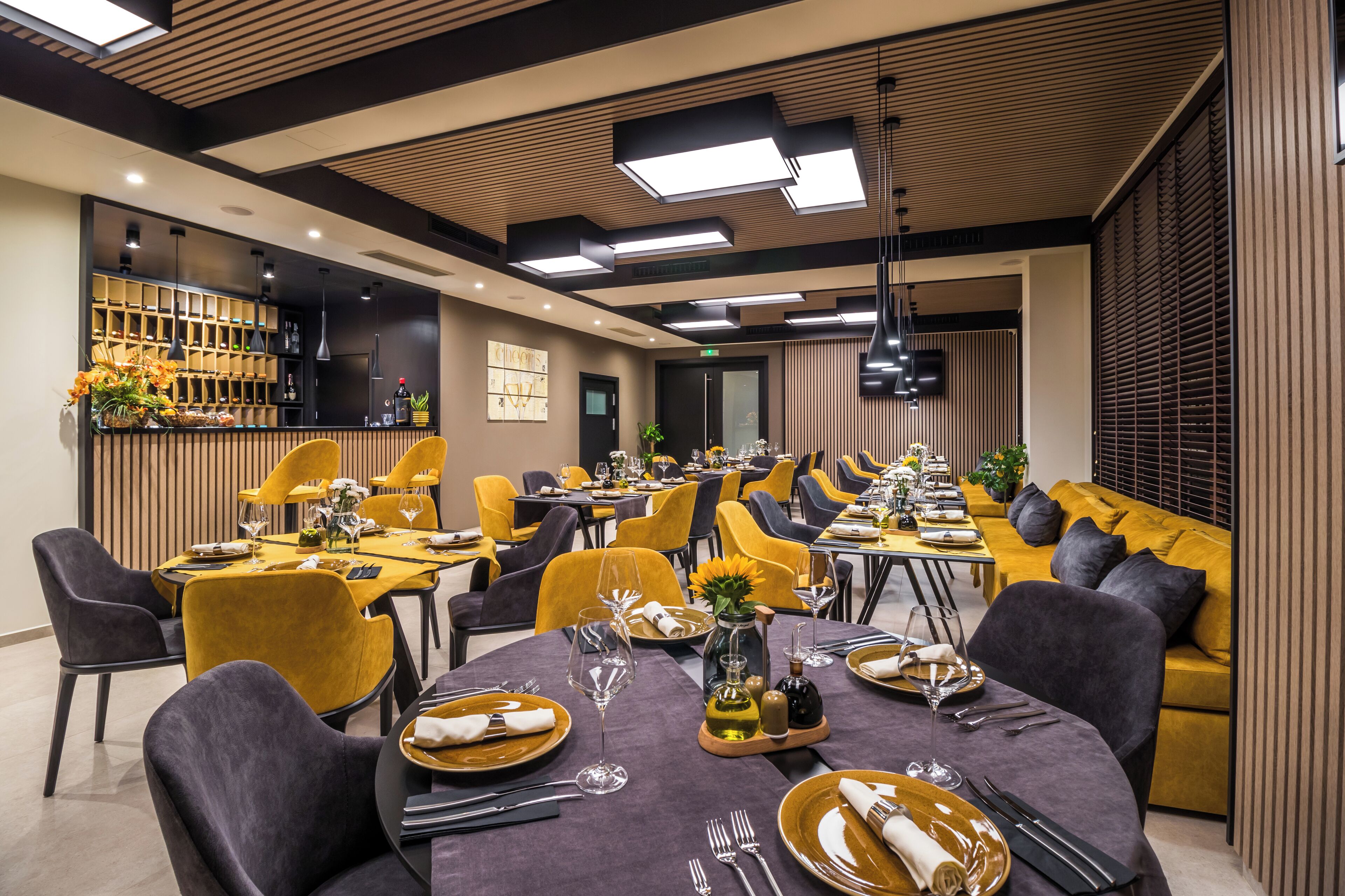 Ein moderner Essbereich mit runden Tischen, gelben Stühlen und einer Bar mit Regalen.