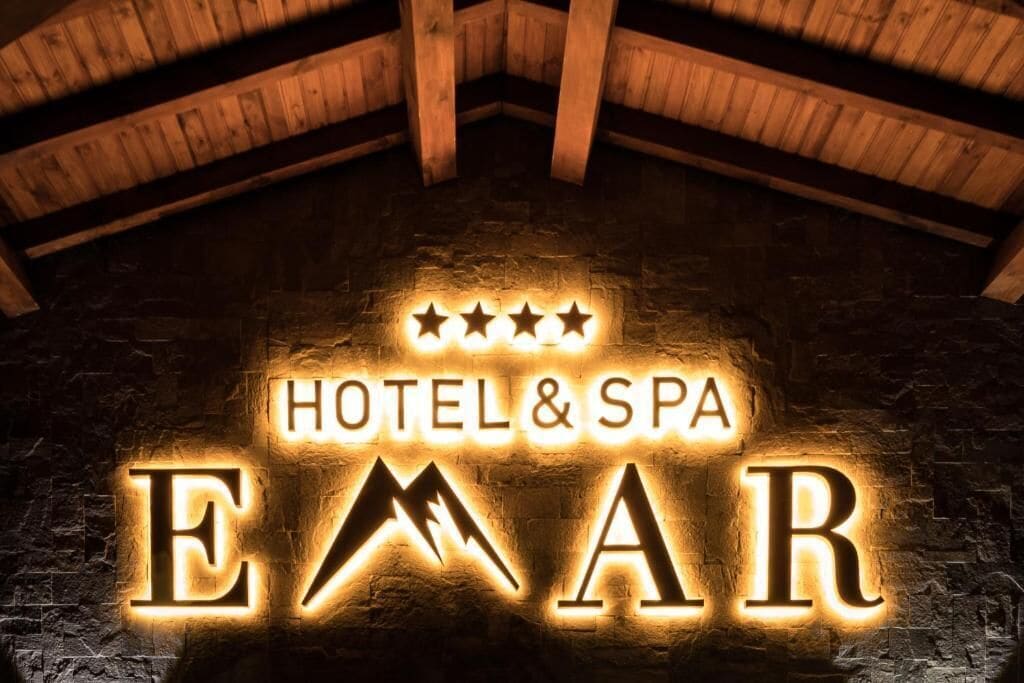 A sign for a hotel and spa named "EMAR" with a rustic wooden ceiling and stone wall background.