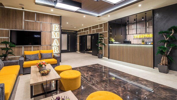 Un hall d’hôtel moderne avec un comptoir d’accueil, un espace salon et une enseigne indiquant la présence d’un restaurant.