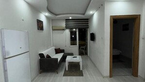 A modern living room with a sofa, a coffee table, and a refrigerator. - Acar apart otel (Antalya)