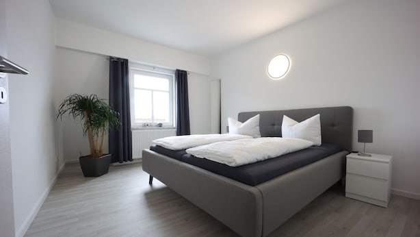 A modern bedroom with a large bed, bedside tables, a potted plant, and a window with curtains.