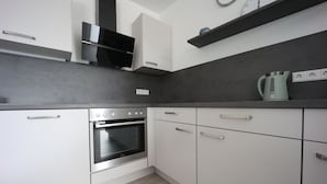 A modern kitchen with white cabinets, a built-in oven, and a kettle on the countertop.