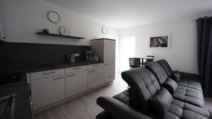 A modern kitchen with white cabinets, a black countertop, and a dining area with a black sofa and a table.