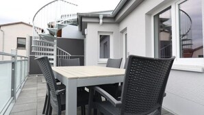 A rooftop terrace with a table and chairs, a spiral staircase, and a view of the city.