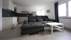 A modern living room with a sectional sofa, a white coffee table, and a kitchen area in the background.
