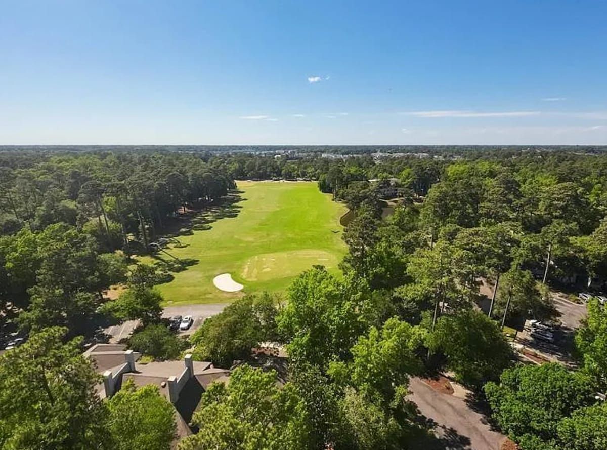 A golf course surrounded by trees and residential buildings.