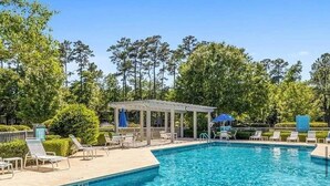 Ein Pool mit Liegestühlen und Sonnenschirmen, umgeben von Bäumen.