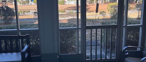 Une véranda avec vue sur un quartier résidentiel, un tapis à motifs et du mobilier d’extérieur.