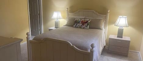 A bedroom with a bed, two bedside tables, a nightstand, a door, and a dresser.