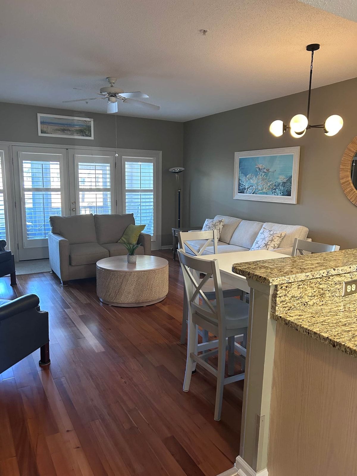 A living room with a ceiling fan, a dining area with a table and chairs, and a kitchen counter.