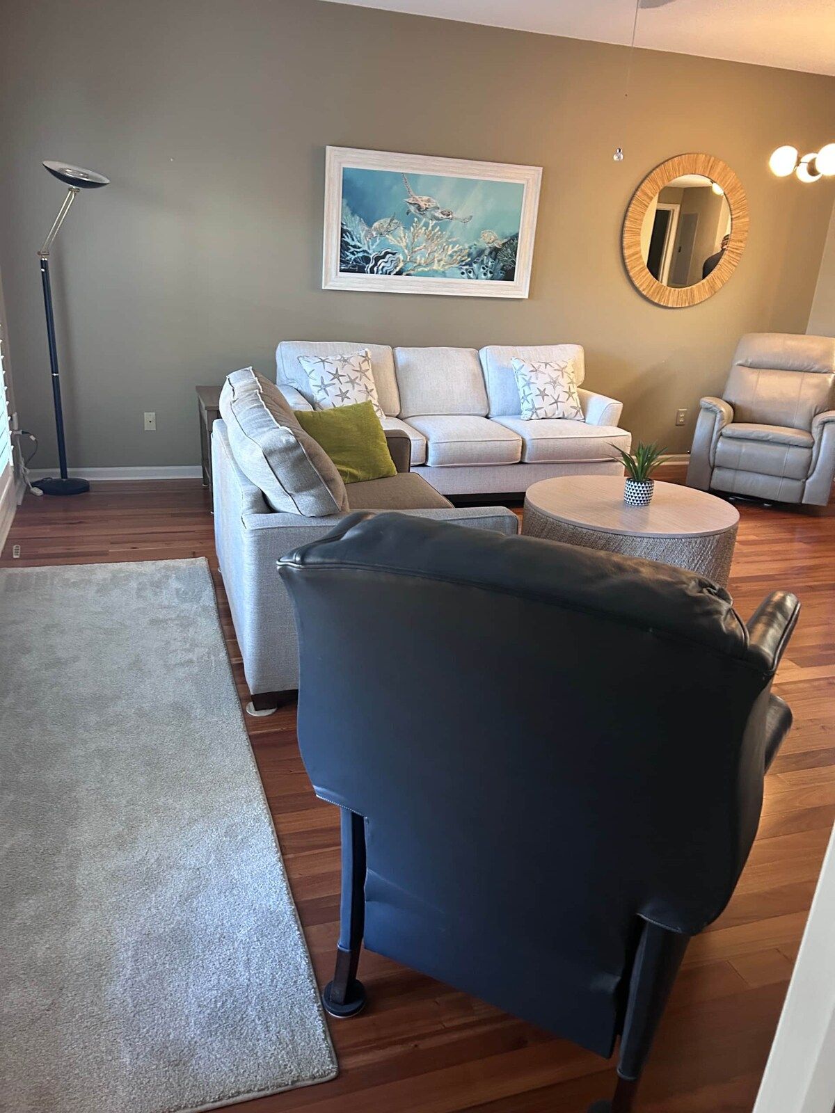 A living room with a sofa set, a coffee table, a black armchair, a floor lamp, and a painting on the wall.