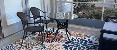 A covered patio area with a table and chairs, a patterned rug, and a view of the house and garden.