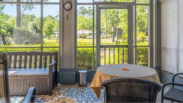 Eine überdachte Terrasse mit Tisch, Stühlen und einer Bank, mit Blick auf einen Park.