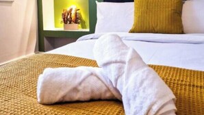 A neatly made bed with white linens and a yellow throw blanket, a dark headboard, and green walls with shelves displaying decorative items.
