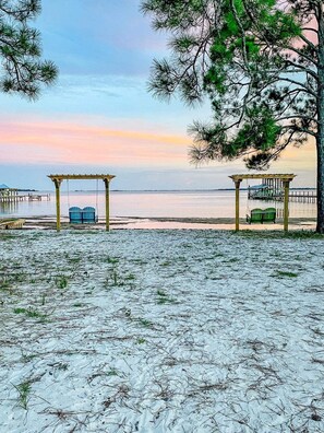 A beach with two wooden gazebos, a clear view of the water, and a distant pier. - Pet Friendly-Salty Breeze on the Bay (Panama City)