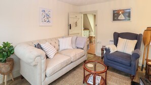 Una sala de estar acogedora con un sofá color beige, un sillón azul, una mesita redonda y una lámpara de pie de mimbre.