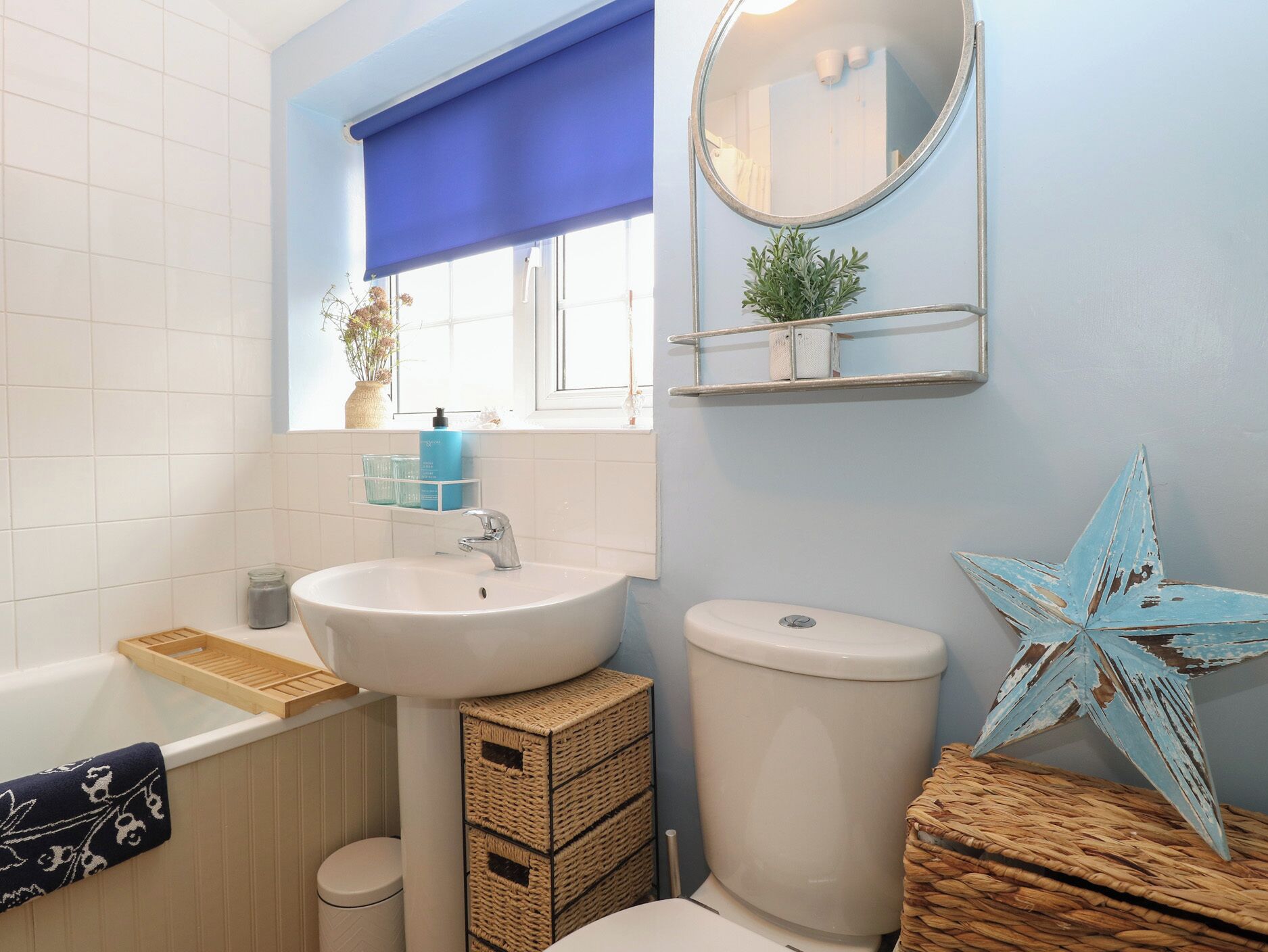 A bathroom with a white sink, a toilet, a bathtub, a blue window blind, a mirror, and a star decoration.