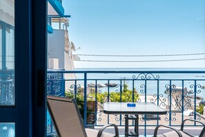 Ein Balkon mit Tisch und Stühlen, mit Blick auf ein Gewässer und ein Gebäude mit blauer Brüstung.
