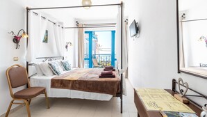 Quarto com cama, cadeira, mesa, televisão e varanda com guarda-corrimão azul.
