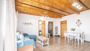A spacious living area with a wooden ceiling, a sofa, a dining table with chairs, and a small table with books.