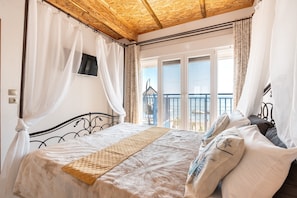 Ein Schlafzimmer mit Bett, Vorhängen, einem Fernseher und einem Balkon mit Blick.