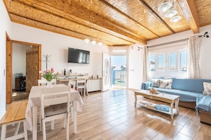 Ein geräumiges Wohnzimmer mit Holzboden, einer Couch, einem Couchtisch und einem an der Wand montierten Fernseher.