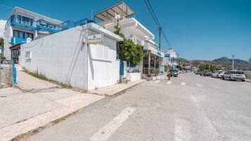 A coastal street with white buildings, a blue balcony, and a clear sky.