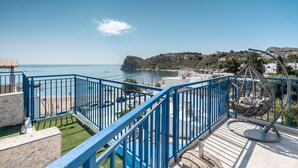 A balcony with a clear view of the sea, a hanging chair, and a blue railing.