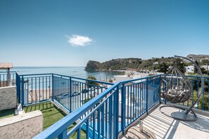 Ein Balkon mit freiem Blick aufs Meer, einem Hängestuhl und einem blauen Geländer.
