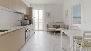 Een moderne keuken met een magnetron, oven en spoelbak, een zithoek met een tafel en stoelen, en een bank.