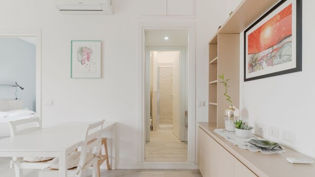 Een moderne keuken met witte kasten, een eethoek met een witte tafel en stoelen, en een gang naar een andere kamer.