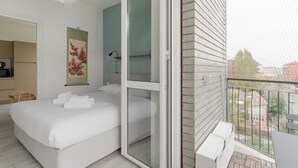 Een slaapkamer met een bed, een schuifdeur naar een balkon, een keukenhoek en een kunstwerk aan de muur.