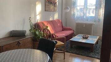 Un salon avec une table ronde, un canapé rouge, une horloge et une affiche accrochée au mur.