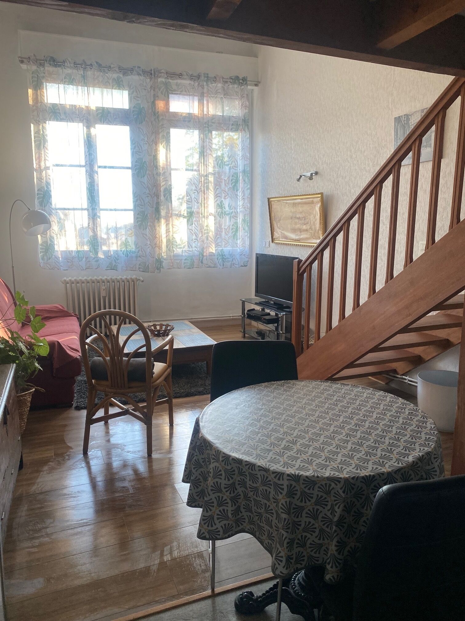 Una sala de estar acogedora con una escalera de madera, una mesa de comedor con mantel estampado, un televisor y un radiador.